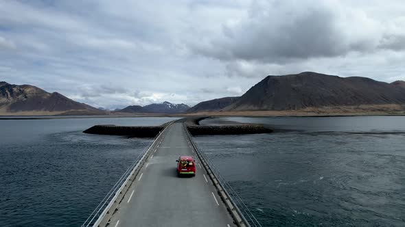 Red car driving over sword shaped bridge in Iceland