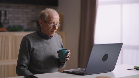 Grandfather is Communicating By Video Call Sitting Alone at Home Kitchen Waving Hands to Web Camera