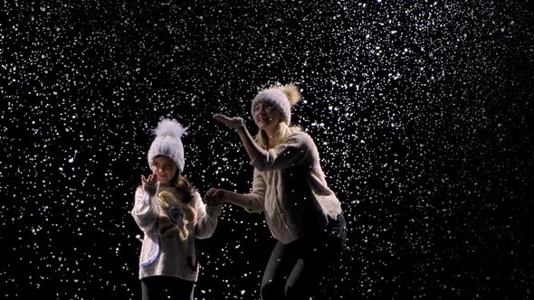 Joyful Smiling Mom and Little Girl Rejoice at the First Snow. Happy Family in the Studio on a Black