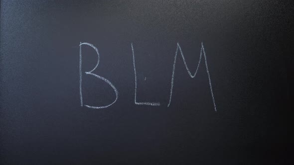 Hand writing BLM with white chalk on blackboard.