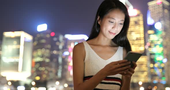 Woman looking at mobile phone in the city at night 