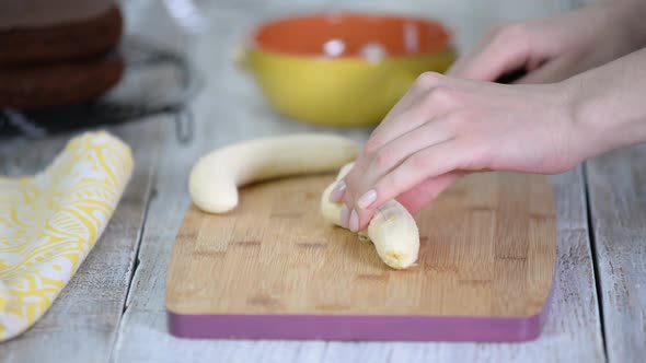 Close-up on woman cutting banana on cutting board.