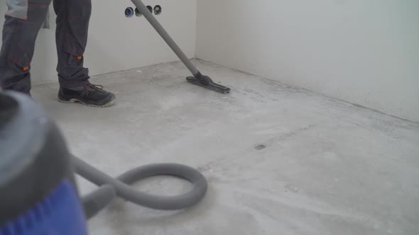 A worker is cleaning a public concrete floor with a vacuum cleaner. 