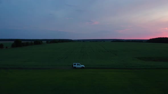 Aerial View of a Car Driving in Nature on a Field at Sunset