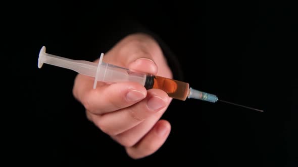hand with a syringe with a drug appears from the darkness, as if offering a dose