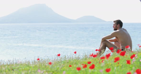 The Handsome Man Sits on a Glade Before the Sea a Lot of Flowers of Poppies Picturesque Sea