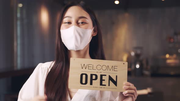 Business owner attractive young asian woman in apron hanging we're open sign