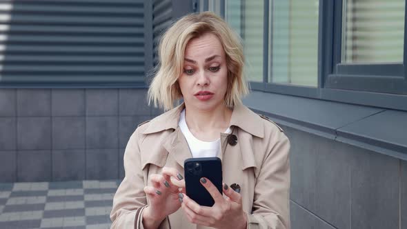 Shocked Business Woman Looking with Surprise at the Smartphone Screen and Covers Her Mouth with Her