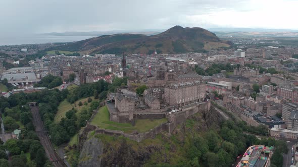 Dolly forward pan down drone shot of Edinburgh castle with king arthurs seat in the background