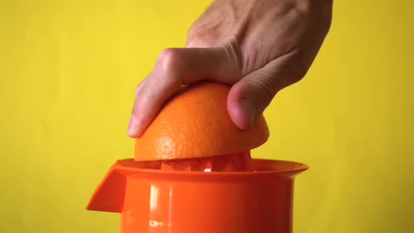 Hand squeezing an orange in manual juicer.