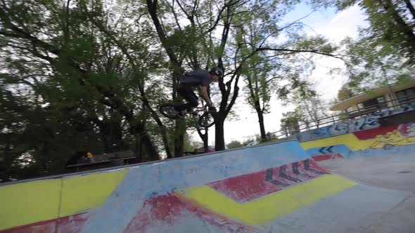 A young man rides a BMX bicycle in a concrete skate park.