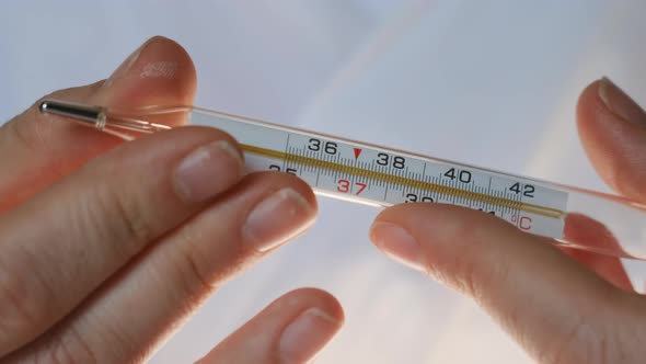Female Doctor Shows Mercury Thermometer to Camera on Which We See Temperature of 36