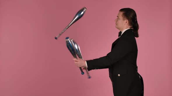 Side View of Professional Circus Artist Masterly Juggles with Clubs in the Studio on a Pink