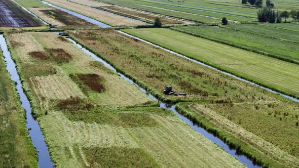 Tractor on Dutch farm land mows lush meadow; aerial half-orbit