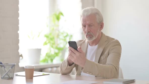 Old Man Browsing Internet on Smartphone in Office