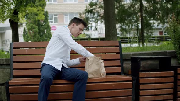 Young Man in Suit Leaves Smartphone on Bench Gets a Hamburger and Eats