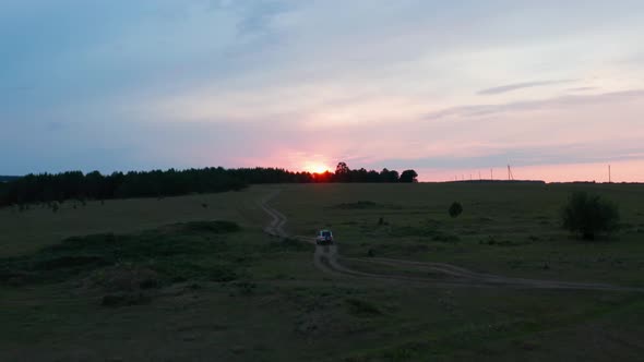 Aerial View of a Car Driving in Nature on a Field at Sunset