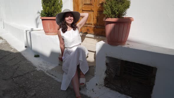 Portrait of Cheerful Beautiful Young Woman Sitting on Stairs at Porch in Ancient City Smiling