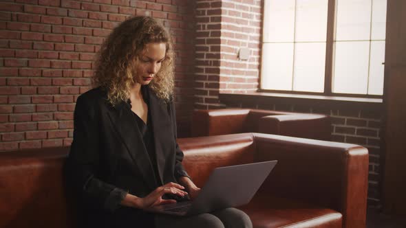 Young Stylish Businesswoman Working on a Laptop in a Loft Apartment with Red Brick Wall