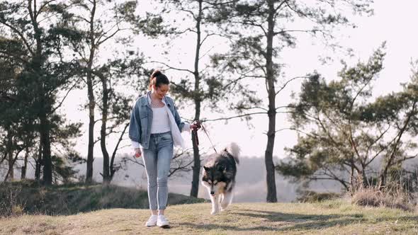 Pretty Girl Is Walking with a Cute Fluffy Dog in the Field