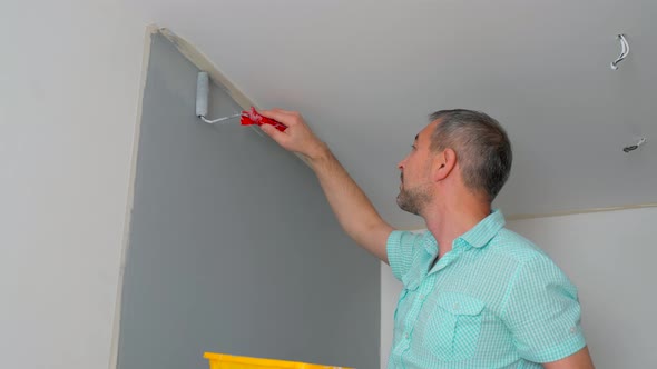 A Man in a Shirt Paints the Walls with a Roller Gray