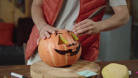 A Young Man in Red Vest Carves Brows of a Halloween Pumpkin