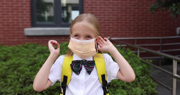 Happy Little Caucasian Blonde Girl Seven Years Old in Uniform with Yellow Backpack Standing Near