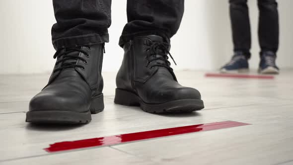 People standing in line behind red tape floor markings for social distance