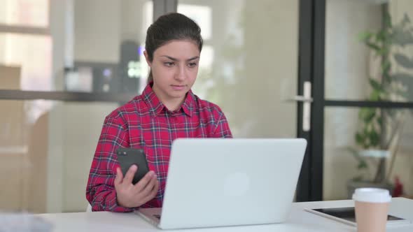 Indian Woman Using Smartphone While Working on Laptop