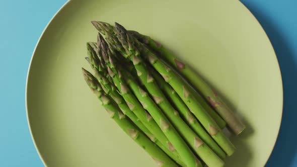 Video of fresh asparagus on green plate over blue background