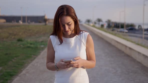 Smiling Young Woman Using Smartphone While Walking on Alley