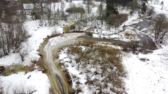 Aerial drone view of a river meandering around a corner in the winter forest. Recorded in Vahiküla F