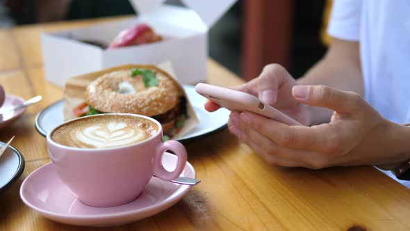 Close Up Of Woman's Hands Using Mobile Smart Phone Sitting In Cafe With Cup Of Coffee