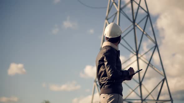 Constructor Inspect High Voltage Tower. Engineer In Hard Hat Maintenance Electricity Transmission.