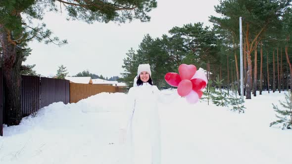 Happy woman throws up heart-shaped balloons outdoor in winter with snow