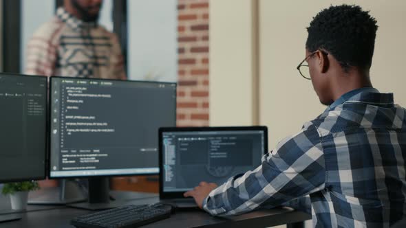 Focused Software Developer Writing Code on Laptop Looking at Multiple Screens with Programming