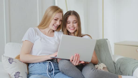 Adult Mother and Teenager Girl Daughter Child Sitting Together on Couch Using Modern Laptop Watching