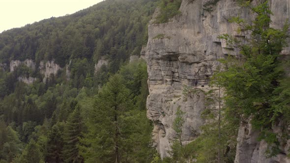 Flying away from a man staying on the edge of a cliff, revealing the via ferrata he was doing to get