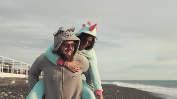 Bearded Man Is Carrying on Back Her Cheerful Girlfriend, Walking Over Sea Coast
