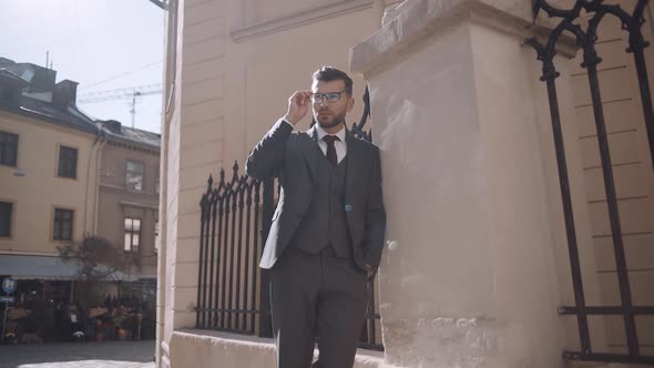 serious businessman walking in suit near modern building. Confident business man in glasses at stree