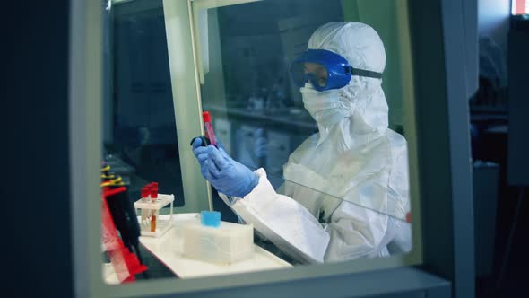 Female Specialist in a Hazmat Suit is Observing Test Tubes