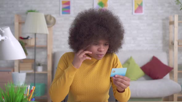 Tired and Stressed African American Woman with an Afro Hairstyle Looking at the Bank Card in His