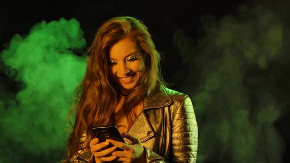 Portrait of Young Pretty Woman Is Joyfully Texting on Her Phone Then Shows Smartphone with a Blue
