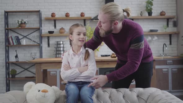 Close-up of Little Teenage Girl with Braided Pigtails Sitting on Sofa and Talking with Bearded