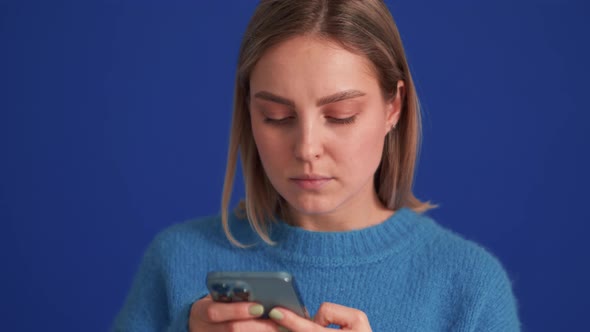 Cheerful woman wearing blue sweater texting by phone