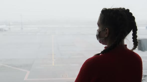 Silhouette of a Masked Young Woman at Airport Terminal Window Looking at Planes