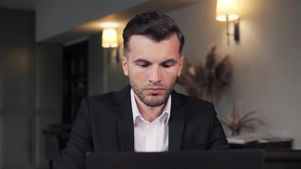 Focused Stylish Businessman Working on Laptop Computer at Hotel Restaurant