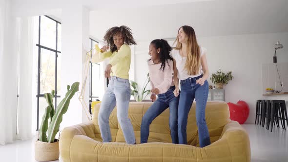 Three Funny Female Friends Dancing Standing on the Sofa Indoors