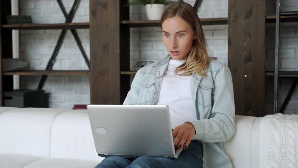 Beautiful Young Woman Is Using a Laptop and Smiling While Sitting on the Sofa at Home