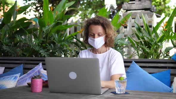 Focused Blonde Freelancer Works on Her Computer with a Face Mask on Her Face alt